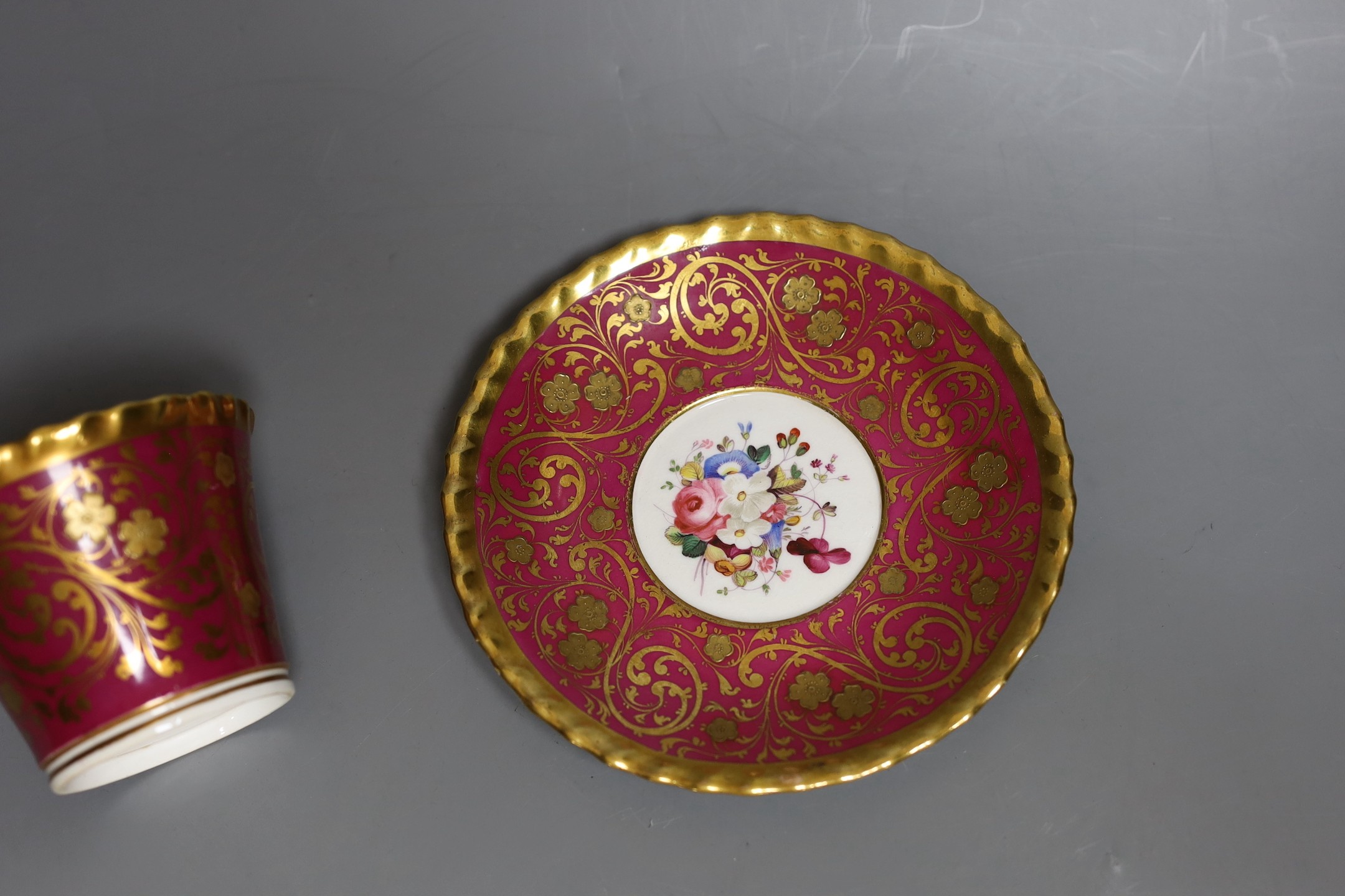 A Chamberlains Worcester superb coffee cup and saucer with crinson ground and elaborate gilding the saucer painted with flowers, the cup painted with flowers in and out, script mark in red to cup